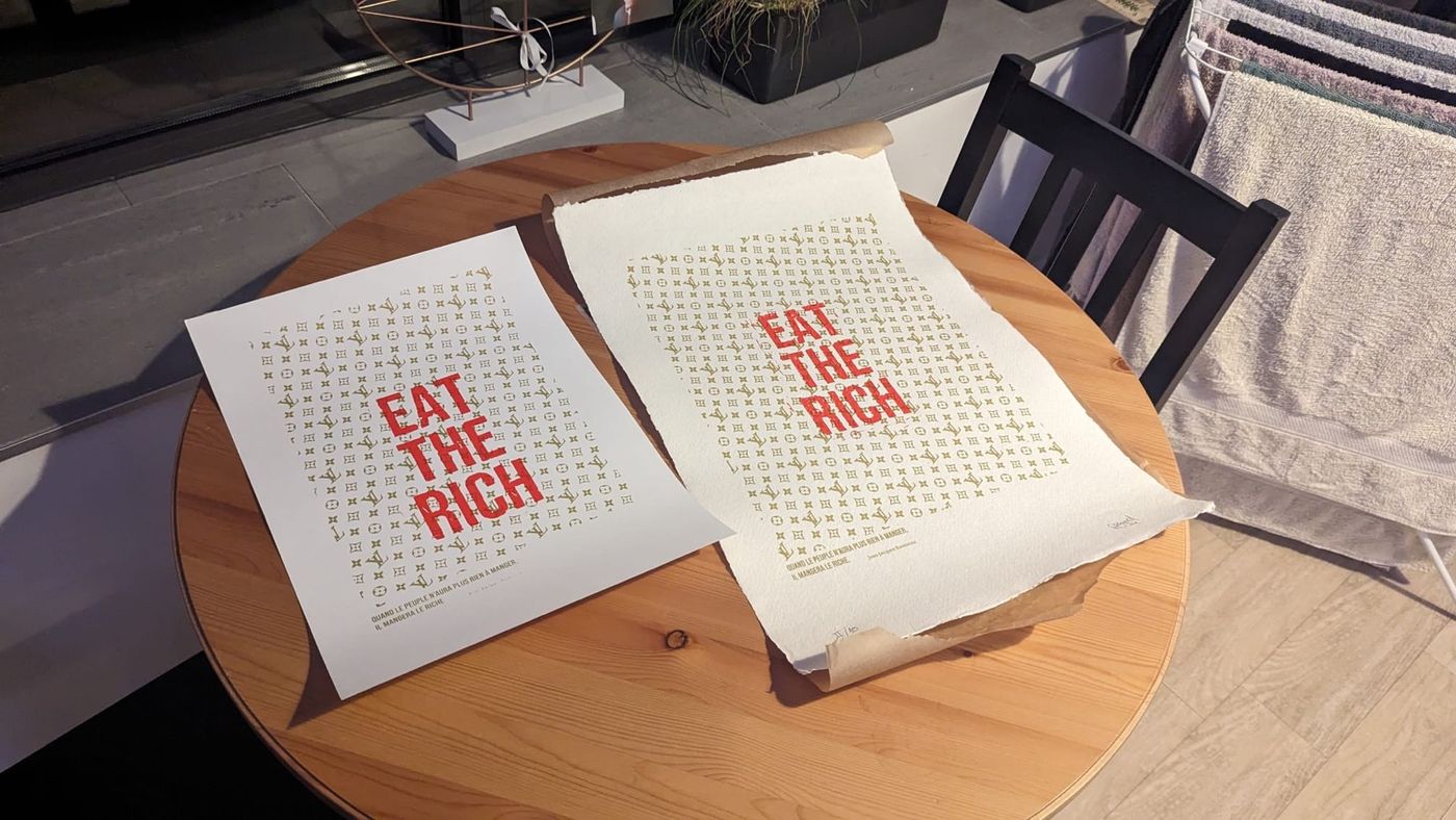 Zwei verschiedene Grafikdrucke auf Papier liegen zum Vergleich nebeneinander auf einer Holzoberfläche.